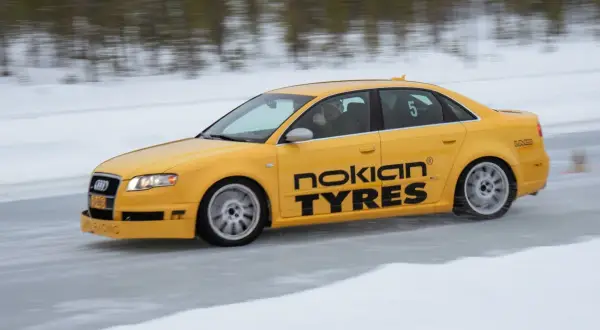 Żółty Audi S1 Quattro z napisem "Nokian Tyres" śmiga po lodowym torze. Kierowca pokazuje kciuk w górę.
