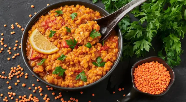 Rote Linsensuppe mit Zitrone und Petersilie, ein gesundes Gericht, das als Fettverbrenner Lebensmittel gilt. Daneben eine Schale roter Linsen.