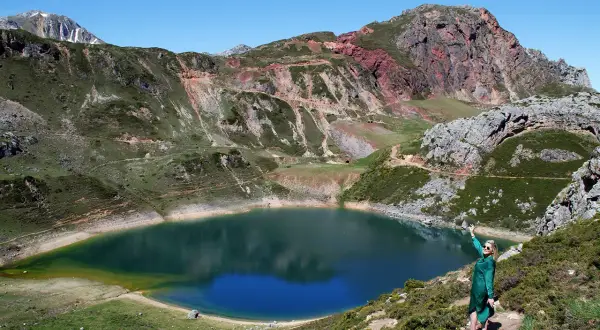 Mujer en la ladera disfruta de las vistas de un lago azul rodeado de montañas, ideal para rutas en Somiedo.