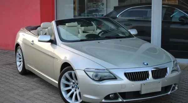 Srebrny kabriolet BMW E64 z beżowym wnętrzem stoi przed salonem samochodowym.