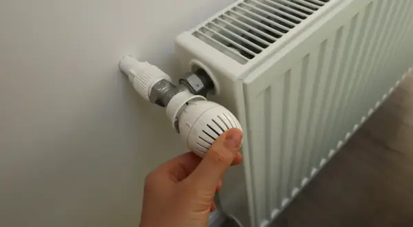 Ręka reguluje termostat grzejnika, gdy zaczynają grzać w blokach.