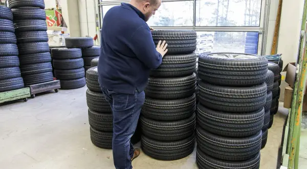 Mężczyzna wybiera najlepsze opony spośród wielu stosów. W magazynie panuje porządek, a opony są ułożone w równych rzędach.