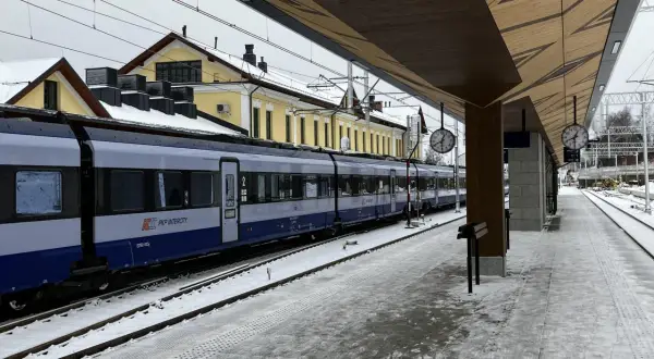 Pociąg PKP Intercity na stacji w Żaganiu, zimowy dzień. Zielona góra w oddali, śnieg na torach i peronie.