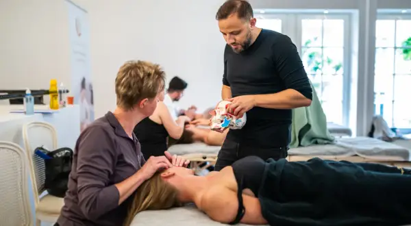 Masaż twarzy: terapeuta pokazuje model czaszki, druga osoba masuje twarz pacjentki.