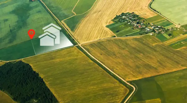 Działka rolna z warunkami zabudowy może stać się działką budowlaną. Widok z lotu ptaka na pola i wyznaczoną działkę z ikoną domu.