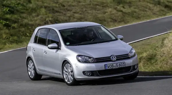 Srebrny Golf 6 R na torze wyścigowym, z kierowcą za kierownicą, pokonuje zakręt.
