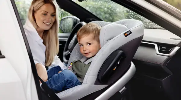 Uśmiechnięta mama patrzy na synka w foteliku na przednim siedzeniu. Czy dziecko może jechać w foteliku na przednim siedzeniu? Tak, jeśli jest odpowiednio zabezpieczone.
