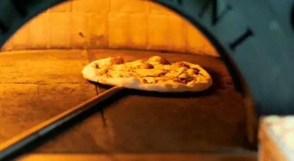 Pizza na łopacie w piecu, gdzie powstała pizza. Ciepło i tradycja wypieku.