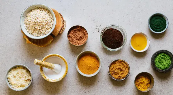 Ingredienser för hemmagjord ansiktsskrubb: havregryn, kakaopulver, kaffesump, gurkmeja, matcha och olja.
