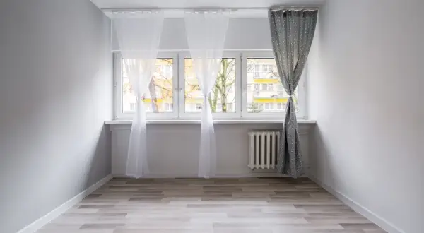 Biały karnisz sufitowy zamontowany nad oknem, na którym wiszą zwiewne firanki i zasłona.