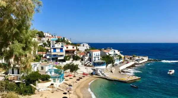En pittoresk kustby på Ikaria, Grekland, med vita hus, en sandstrand och turkost vatten.