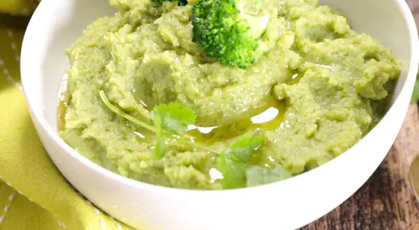 Un bol de purée de brocolis onctueuse, garnie de fleurettes de brocolis et d'un filet d'huile d'olive.