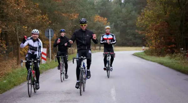 Peleton kolarzy jedzie drogą wśród jesiennych drzew. Czy to wyścig, czy wspólna przejażdżka?
