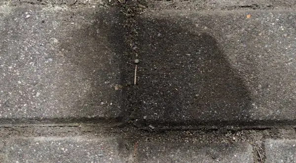 Stare plamy z oleju na kostce brukowej tworzą ciemny, rozlany kształt.