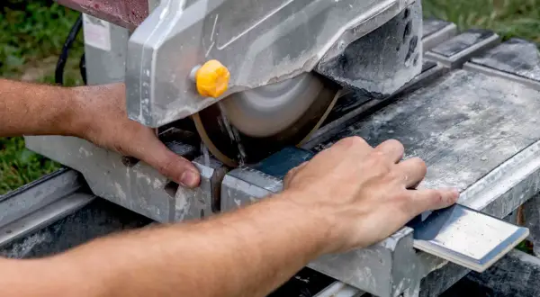 Hands guide a tile across a wet saw, demonstrating how to cut tile that is already installed.