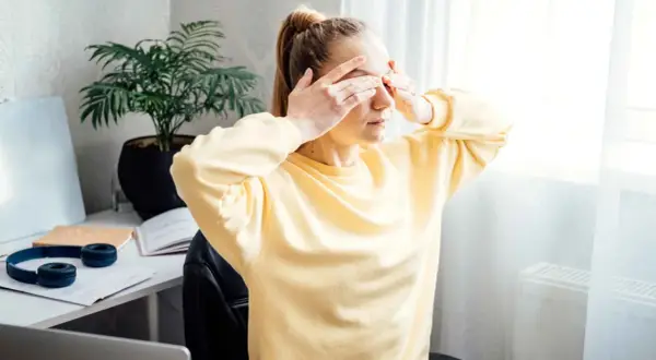 Une jeune femme, le visage marqué par la tension oculaire et le stress, se couvre les yeux.
