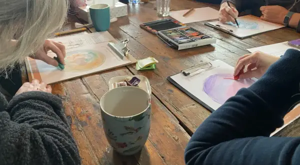 Creatieve workshop voor hsp mensen. Ze tekenen met pastelkrijt op papier, omringd door kopjes en kleurpotloden.