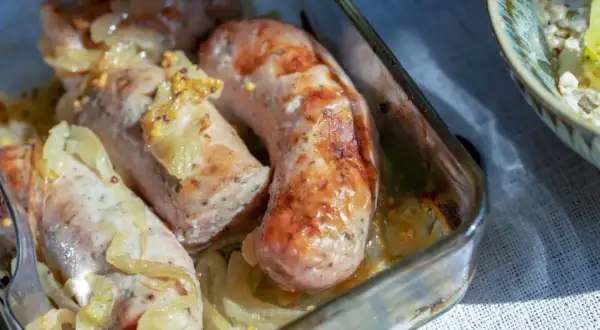 Soczysta biała kiełbasa pieczona z cebulą i musztardą w szklanym naczyniu.
