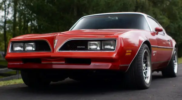 Röd Pontiac Trans Am från 70-talet, med sina karaktäristiska dubbla strålkastare och en ikonisk grill.