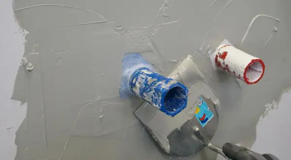Mit einer Kelle wird graue Masse aufgetragen, um die Rohre in der Wand zu dusche abdichten.