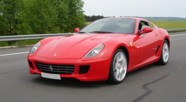 Czerwone Ferrari 599 pędzi po drodze, otoczone zielenią.