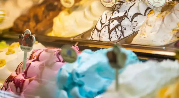 Verschiedene Eissorten in einer Auslage, darunter ein cremiges gelbes Eis, Stracciatella und ein fruchtiges Eis.