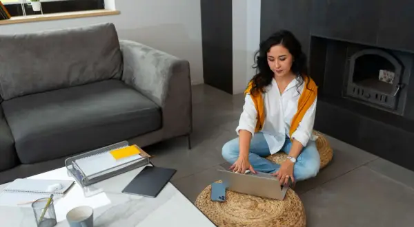 Mujer trabajando en portátil en el salón, pensando si puedo alquilar mi vivienda habitual.