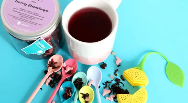 Kolorowa kompozycja z herbatą dla dzieci "Berry Flamingo". Sześć małych łyżeczek z suszem owocowym, kubek z naparem i urocze akcesoria do parzenia.