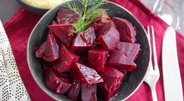Schüssel mit gewürfelten, glänzenden roten Rüben, die man roh essen kann, garniert mit Dill. Daneben Kartoffelpüree und Besteck.
