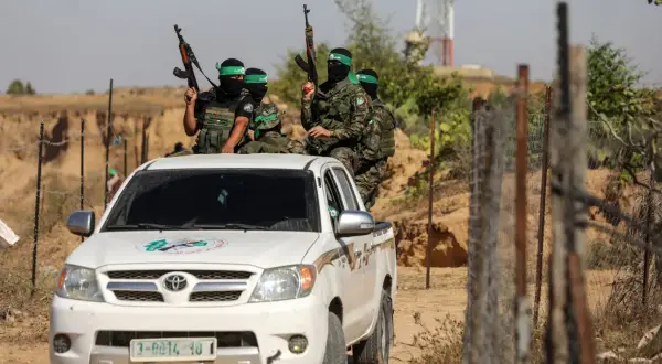 Uzbrojeni bojownicy Hamas w zielonych opaskach na głowach siedzą na białej toyocie, gotowi do akcji.