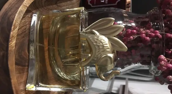 Złoty Kenzo Elephant zdobi flakon perfum, otoczony drewnianą misą i ozdobnymi gałązkami z różowymi owocami.