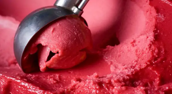 Ein Löffel nimmt eine Kugel leuchtend rotes Eis auf. Es sieht aus wie ein köstliches Eis mit Ei, das auf der Zunge zergeht.