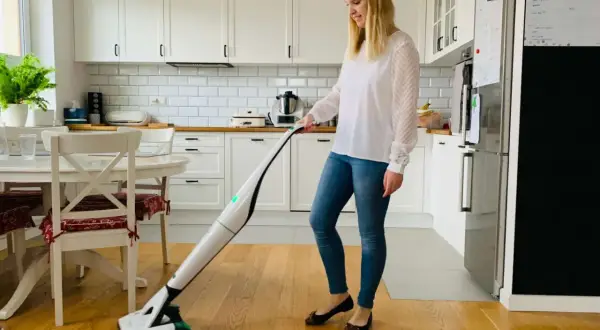 Kobieta sprząta kuchnię nowoczesnym odkurzaczem Vorwerk.