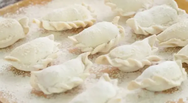 Surowe pierogi, gotowe do gotowania, posypane mąką. Idealne na domowy obiad, zgodnie z tradycyjnym ciasto na pierogi przepisem.