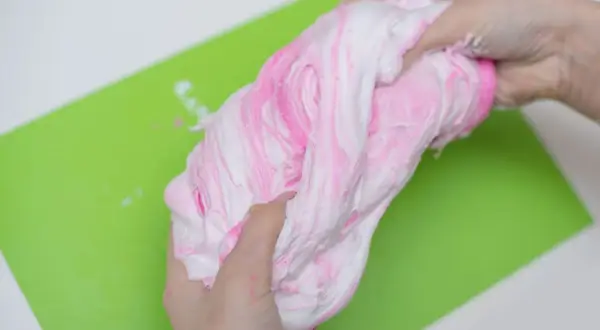 Ręce ugniatają różowo-biały slime, pokazując, jak zrobić slime z kleju i aktywatora.