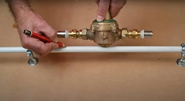 Ajustement d'un réducteur de pression pour comment augmenter la pression d'eau. Un homme marque un tuyau avec un crayon.