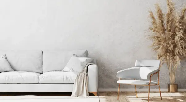 Un salon moderne avec un canapé blanc, un fauteuil design et un bouquet de pampas sur un mur au motif crépis.