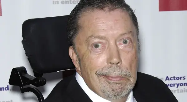 Tim Curry w wózku inwalidzkim, zmagający się z chorobą, ale wciąż z iskrą w oku.