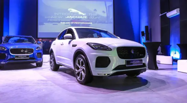 Biały i niebieski Jaguar E-Pace na prezentacji. Na ekranie w tle logo Jaguara i napis "Introducing the new Jaguar E-Pace".