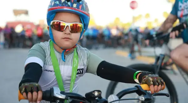 Chłopiec w kasku rowerowym i okularach przeciwsłonecznych, gotowy do jazdy. Czy kask na rower jest obowiązkowy? Ten młody cyklista pokazuje, że bezpieczeństwo jest ważne.