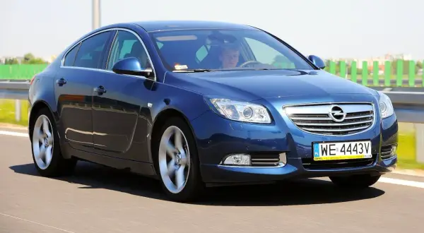 Niebieski Opel Insignia 1.6 Turbo pędzi po drodze. Kierowca wpatrzony w horyzont.