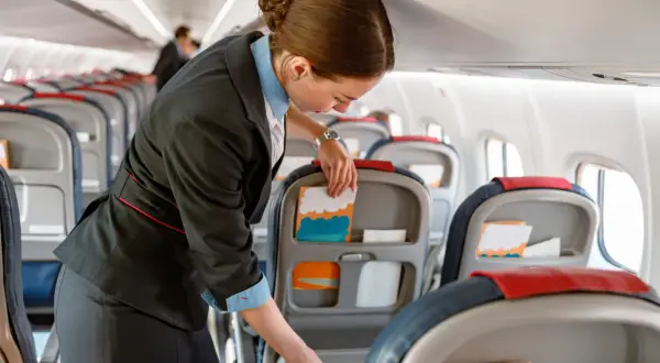 Uśmiechnięta stewardessa przygotowuje kabinę samolotu, układając materiały w kieszeniach foteli.