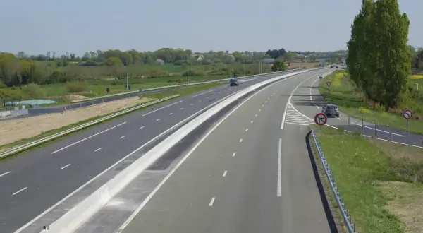 Vue aérienne d'une autoroute avec une voie d'accélération et de décélération, bordée de verdure et de panneaux de signalisation.