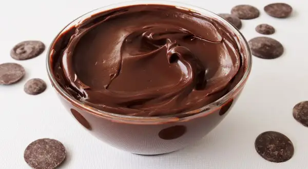 Un tazón de deliciosa crema de chocolate, con trozos de chocolate esparcidos alrededor.