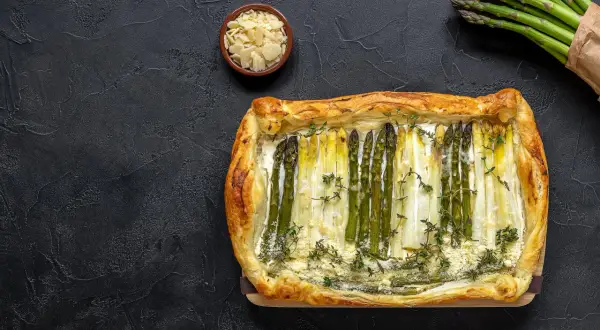 Pyszne szparagi w cieście francuskim, ozdobione tymiankiem i parmezanem, prezentują się apetycznie na ciemnym tle.