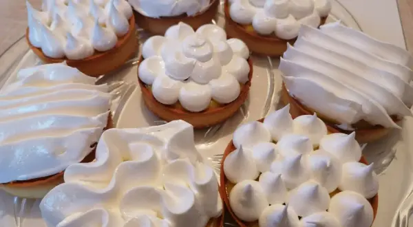 Plusieurs tartelettes garnies d'une crème jaune et surmontées de délicieuse meringue italienne aux formes variées.