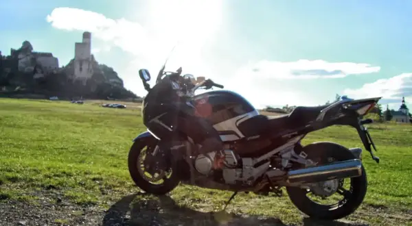 Motocykl na tle zamku i zielonej łąki w słoneczny dzień.
