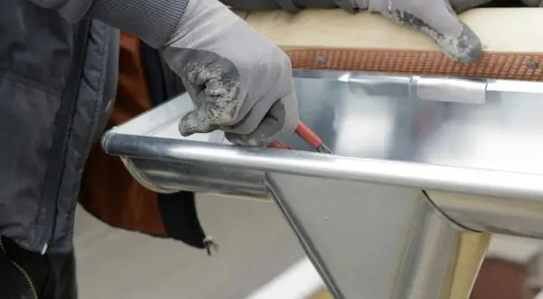 Hand mit Handschuh dichtet mit Werkzeug eine Dachrinne ab.