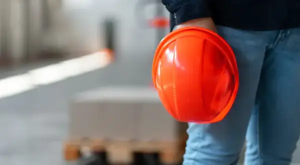 Persona con casco arancione in mano, in un magazzino. Il RSPP quando è obbligatorio garantisce la sicurezza.