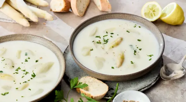 Cremige Spargelsuppe aus Spargelschalen, garniert mit Petersilie. Dazu Baguette und Zitronenspalten.